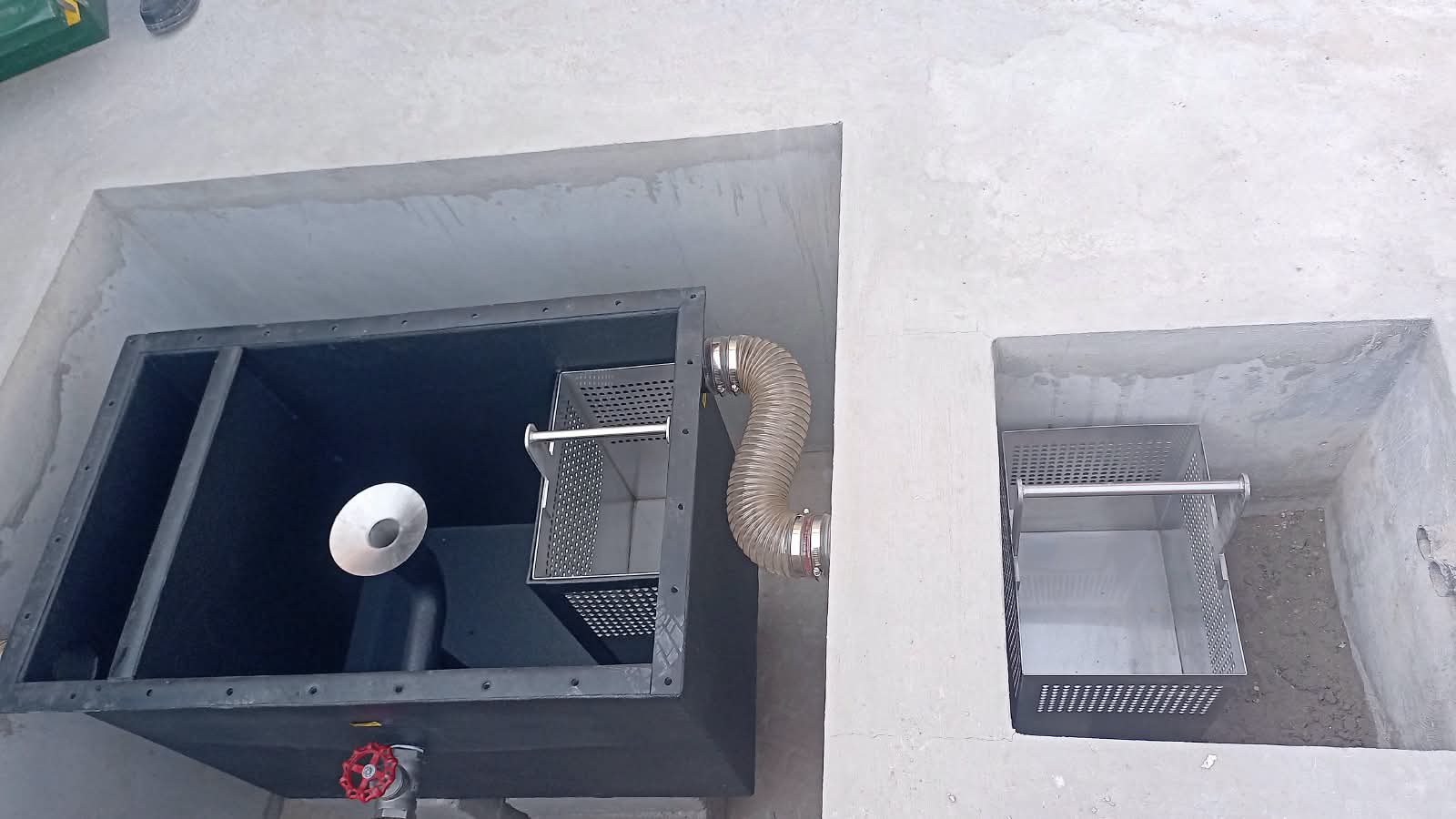 Oil water separator installed in a concrete pit with strainer baskets and connecting hose